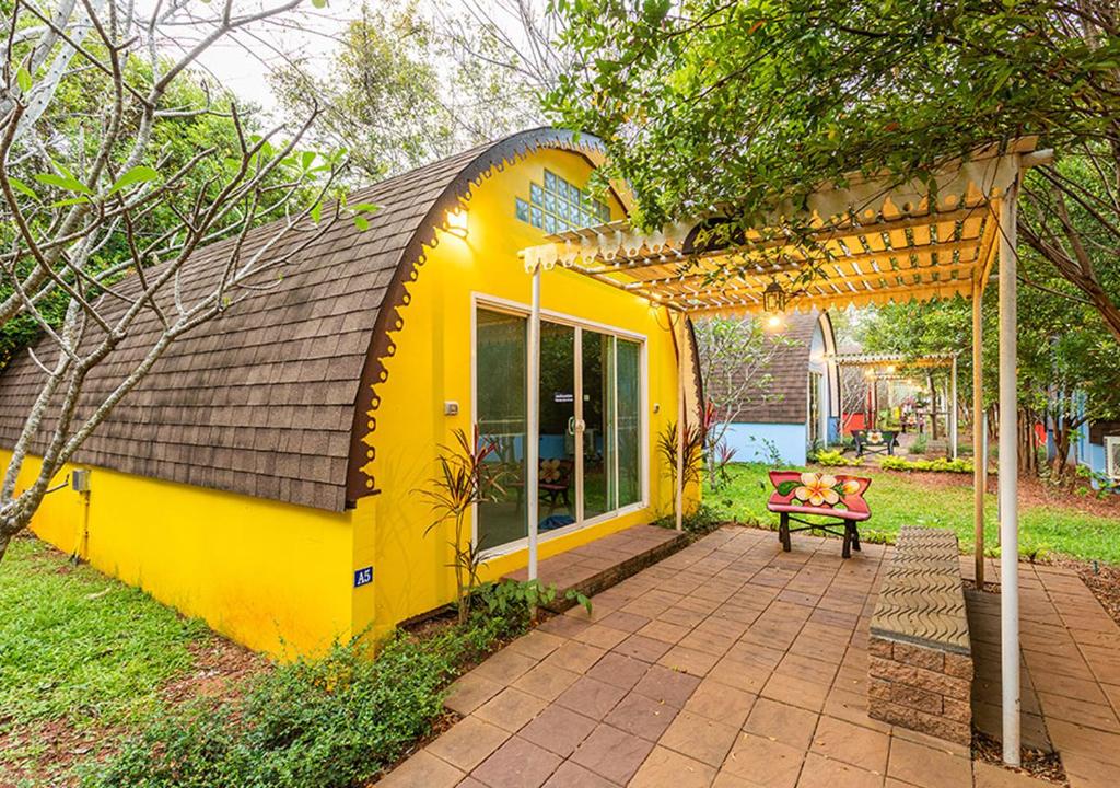 une maison jaune avec pergola et banc dans l'établissement Khao Yai Fantasy Resort, à Nong Nam Daeng