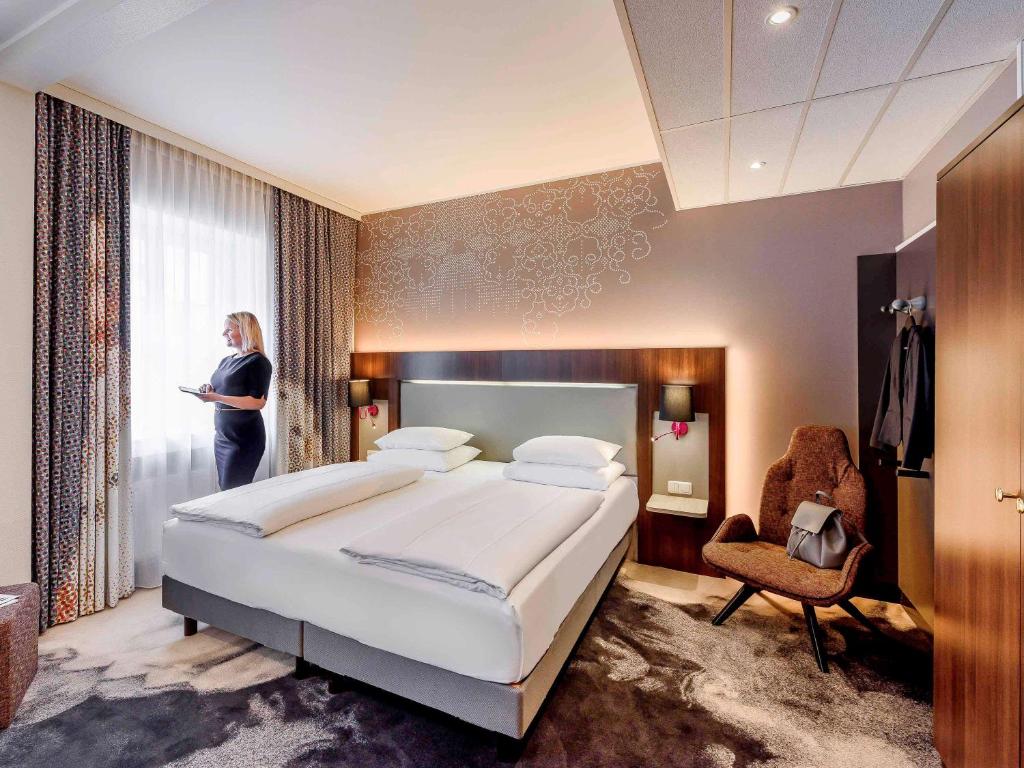 a woman standing in a bedroom with a large bed at Mercure München am Olympiapark in Munich