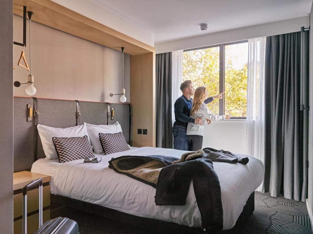 two people standing in a hotel room looking out the window at Assembly Leicester Square in London