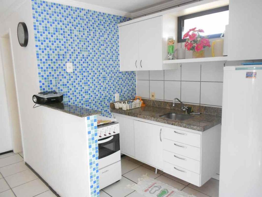a small kitchen with white cabinets and blue tiles at Apartamento Residence Praia Porto Iracema in Fortaleza