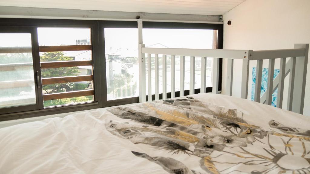a bed in a bedroom with windows and a bedspread at Appartement Cosy Seignosse bord de mer in Seignosse