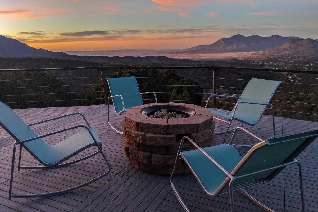 three chairs and a fire pit on a deck with the sunset at Sierra Blanca Mountain Retreat 16 Miles to Ruidoso in Nogal