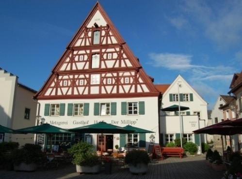 a large building with a pointed roof with tables and umbrellas at Metzgerei Gasthof Romantik Hotel Der Millipp in Beilngries