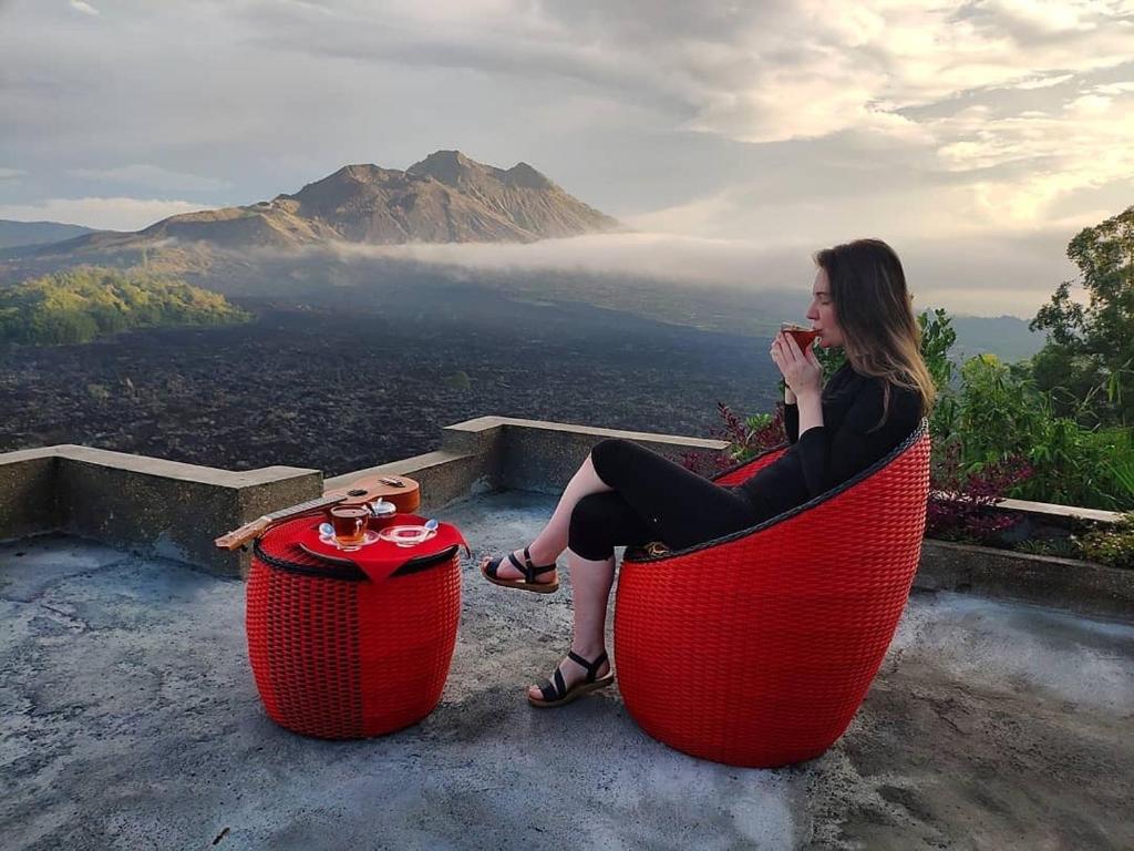 KintamaniにあるAyodya Batur Villaの赤い椅子に座って飲み物を飲む女