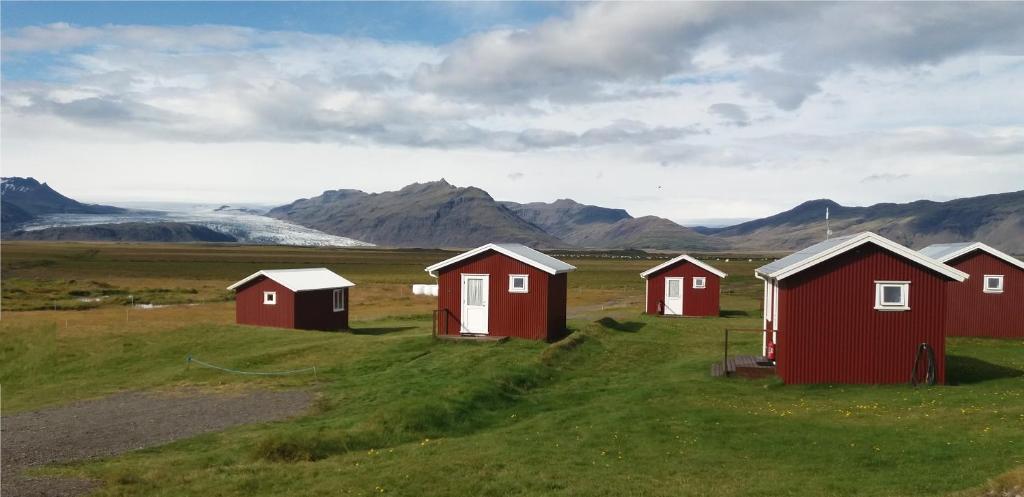 un grupo de casas rojas en un campo con montañas en Lambhus Glacier View Cabins, en Höfn