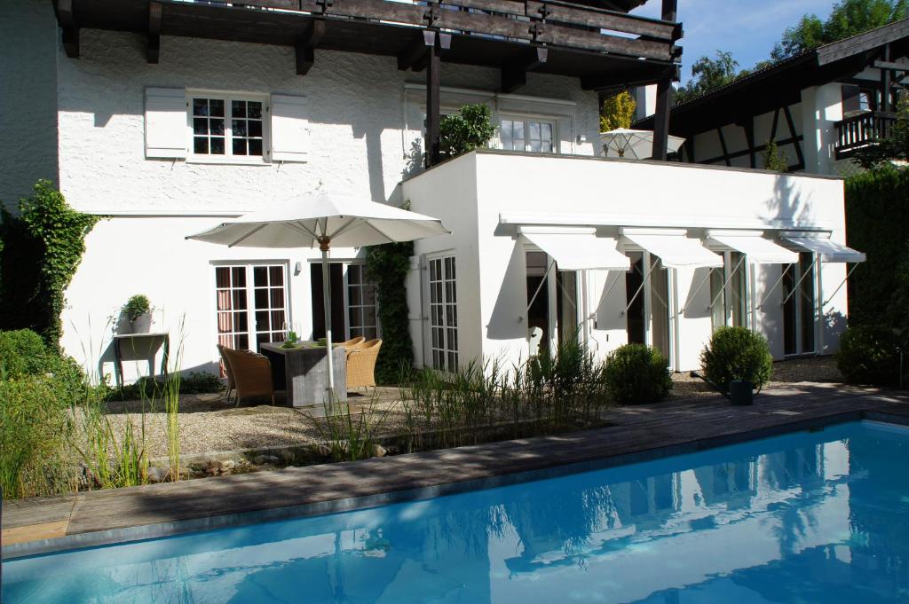 uma casa branca com piscina e guarda-sóis em Landhaus am Plattenbichl - Luxus Apartment mit Privat-Pool und Sauna - im Sommer Bergbahn inklusive em Oberstdorf