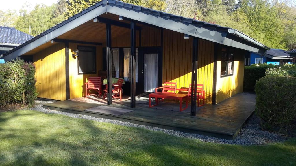 ein Haus mit einer Holzterrasse mit roten Stühlen in der Unterkunft "Ferienanlage AmWalde" Ferienhaus Retro Chalet Nr 1 in Kellenhusen