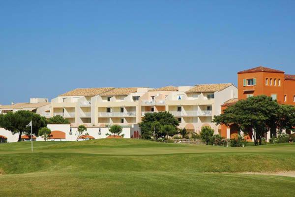 un parcours de golf avec un grand bâtiment et un green dans l'établissement APPART - T3 - 6 PERSONNES – GOLF CAP D’AGDE, au Cap d'Agde
