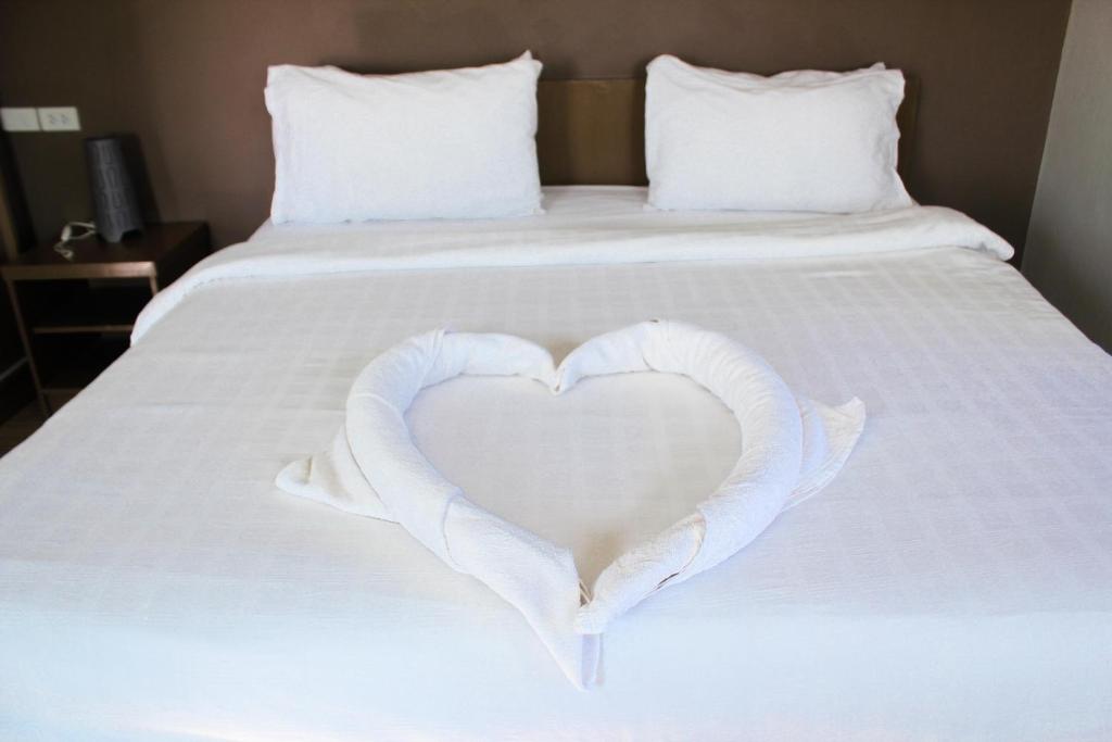 a white heart on a bed with white sheets at Plus Hotel in Loei