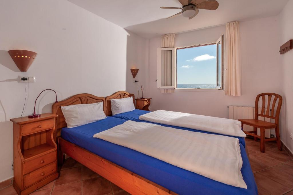 a bedroom with a bed with blue sheets and a window at Residencial Playa Mar in Cala Mendia