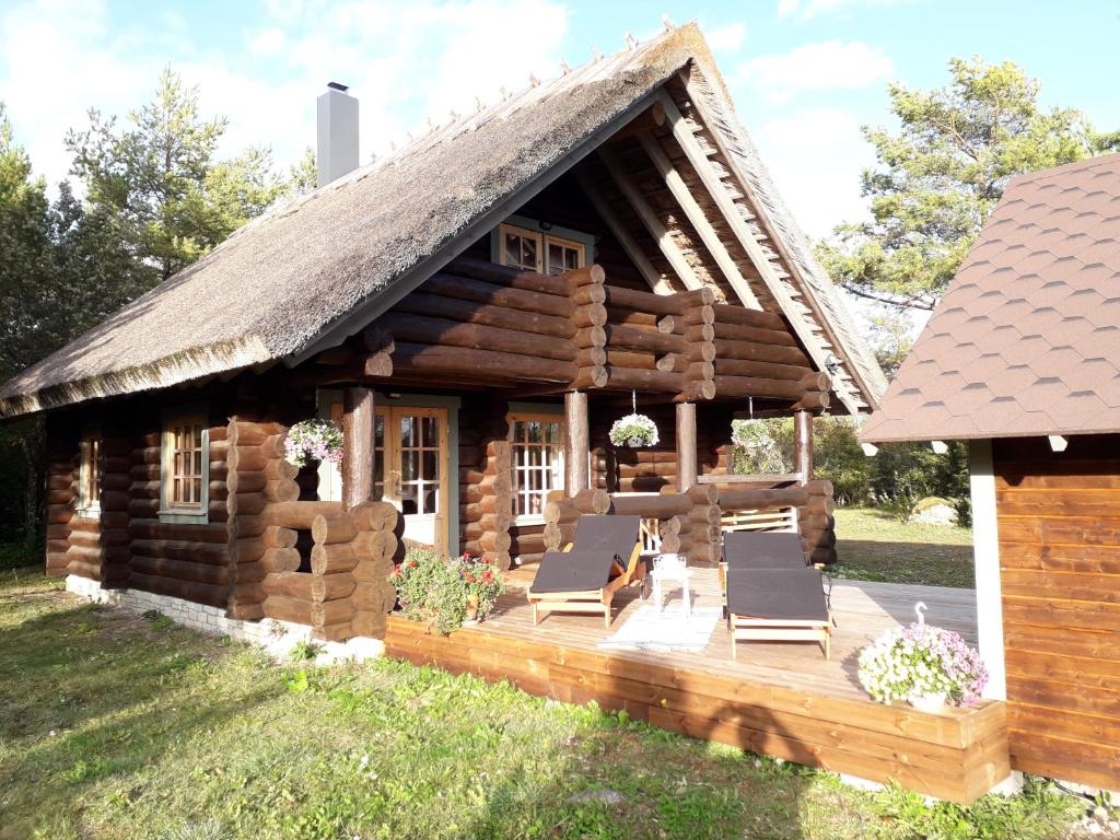 a log cabin with chairs and a deck in the yard at Pähkli Seaside Cottage with Cozy Outdoor Patio in Kõiguste