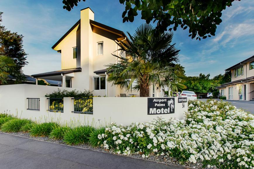 a white fence in front of a house with flowers at Airport Palms Motel in Christchurch