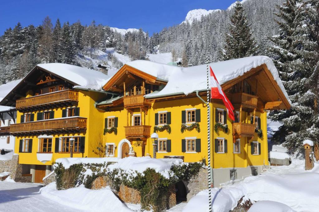 a yellow house in the snow with a flag at Chalet Brunnenhof in Sankt Anton am Arlberg