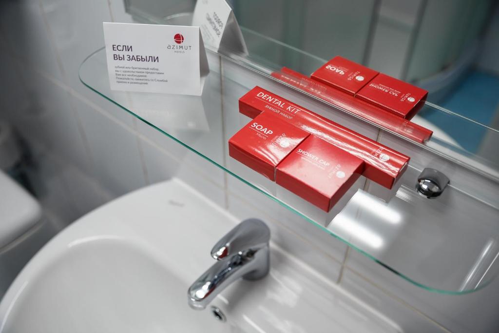 a glass shelf above a sink with red pamphlets at AZIMUT Hotel Kemerovo in Kemerovo