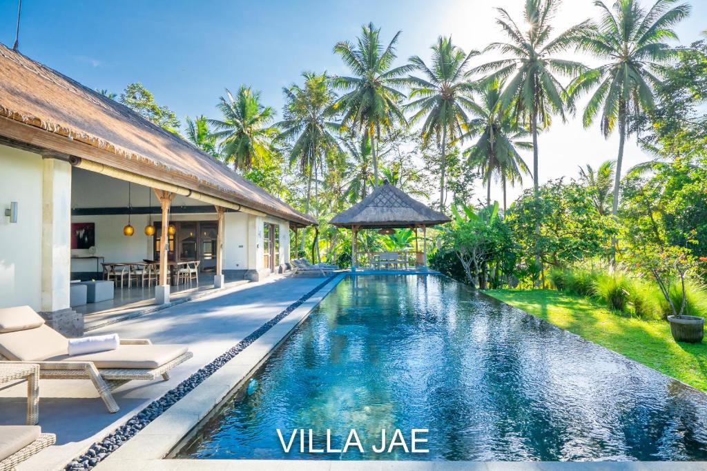 a swimming pool in front of a villa with palm trees at Rouge - Private Villa Jae in Ubud