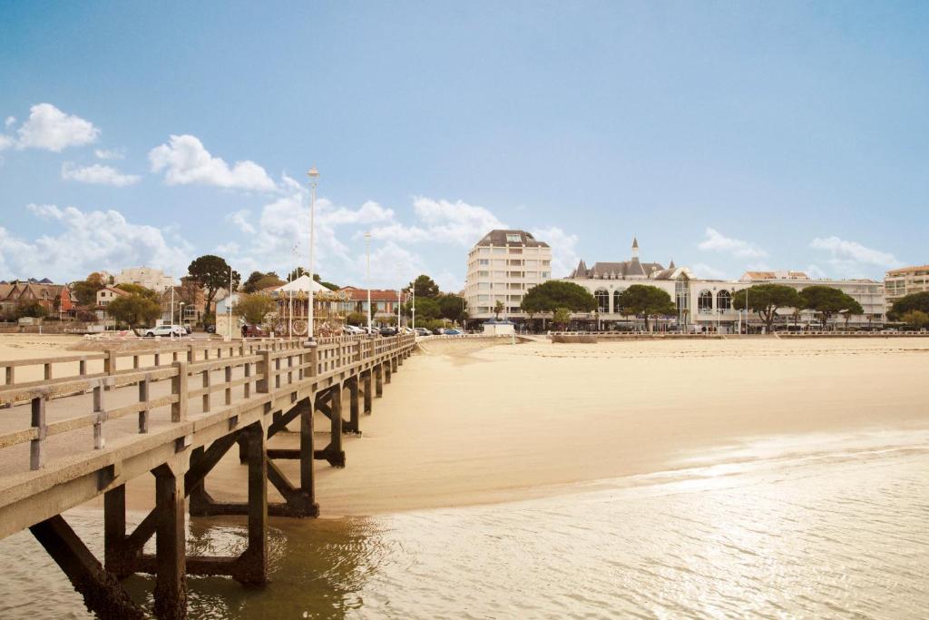 un puente de madera sobre una playa con edificios de fondo en Hôtel Le B d'Arcachon by Inwood Hotels en Arcachon