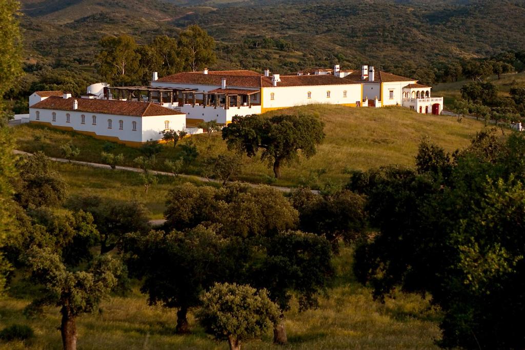 une grande maison blanche sur une colline avec des arbres dans l'établissement Parque de Natureza de Noudar, à Barrancos
