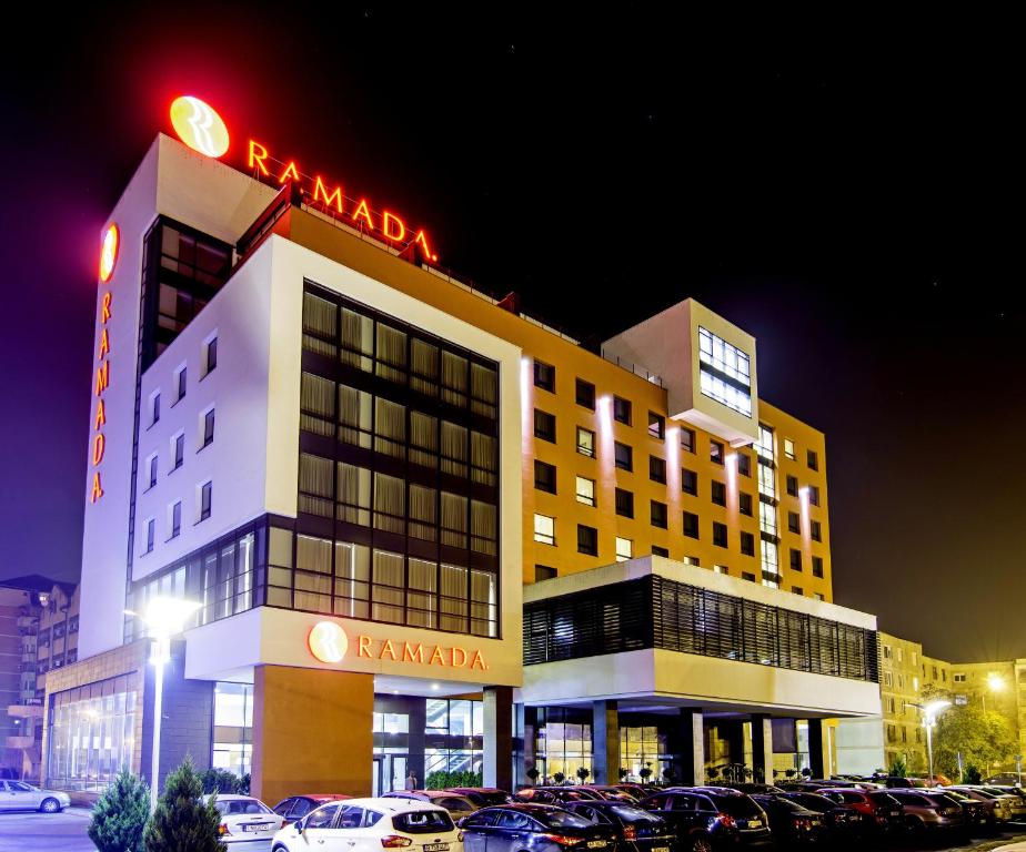 a hotel with cars parked in a parking lot at night at Ramada by Wyndham Oradea in Oradea