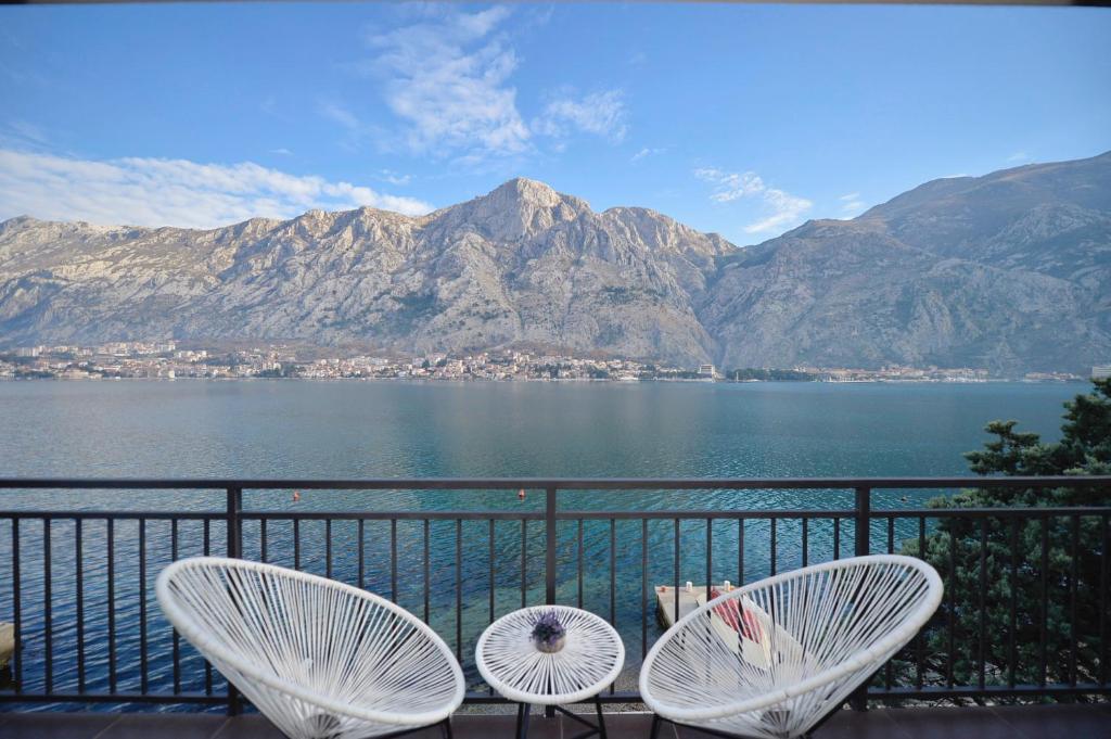 2 sillas blancas en un balcón con vistas a las montañas en House 44 SEAFRONT APARTMENTS, en Kotor