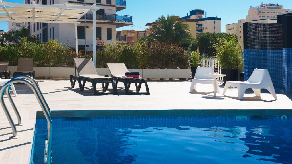 a swimming pool with white chairs and a table and chairs at Hotel Albatros in Gandía