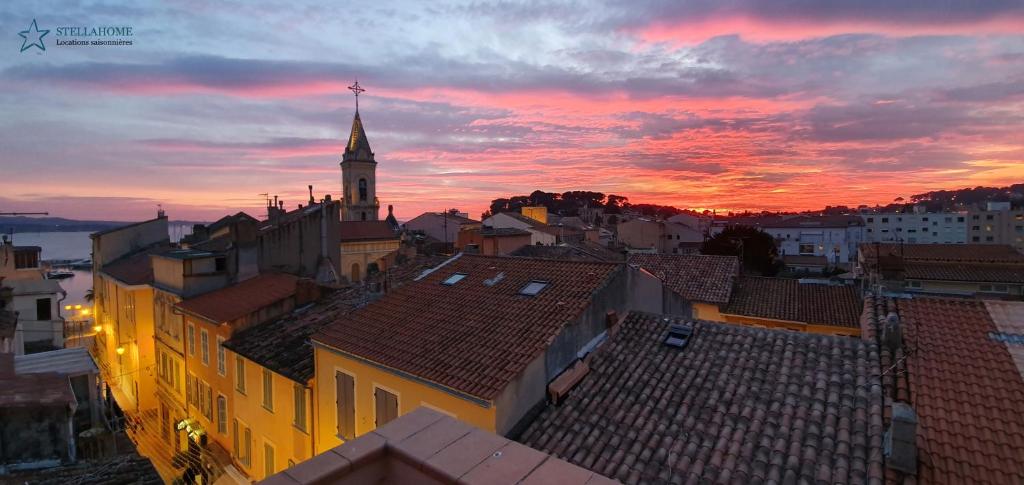 een zonsondergang boven een stad met daken en een kerk bij StellaHome - Sur Les Toits in Sanary-sur-Mer