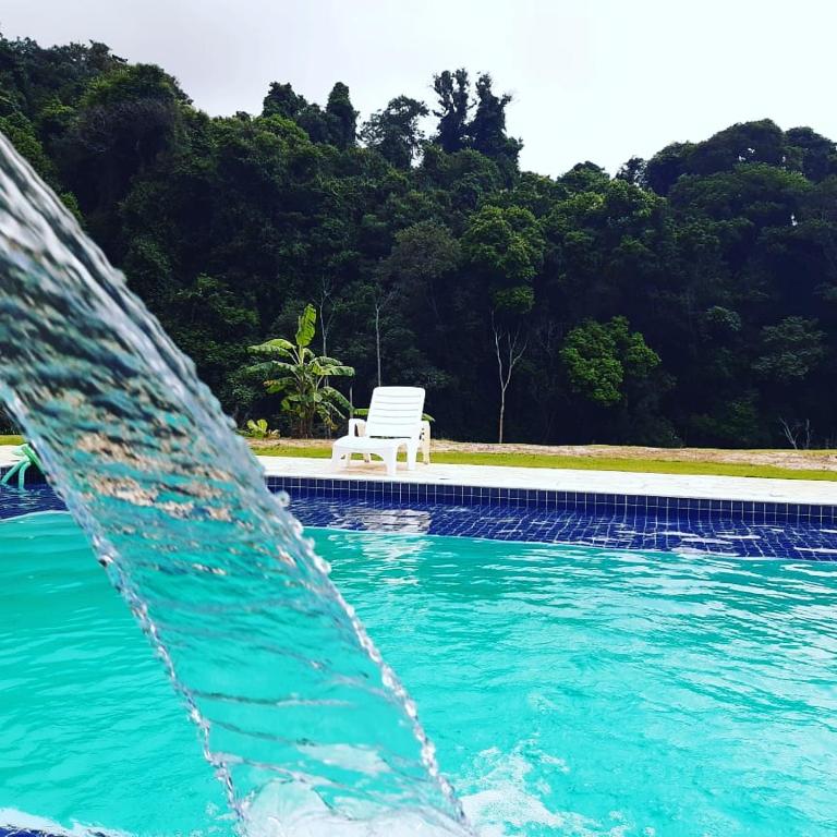 a fountain in front of a swimming pool with a bench at Recanto Das Borboletas in São Roque