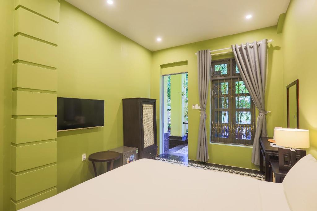 A green bedroom viewed from the bed, with a TV, wardrobe and window-side desk.