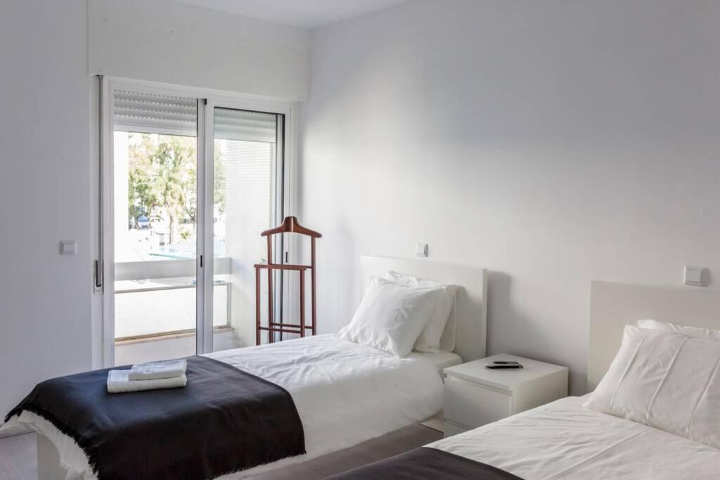 a white bedroom with two beds and a window at REMODELED APARTMENT IN THE CITY CENTER. (FARO) in Faro