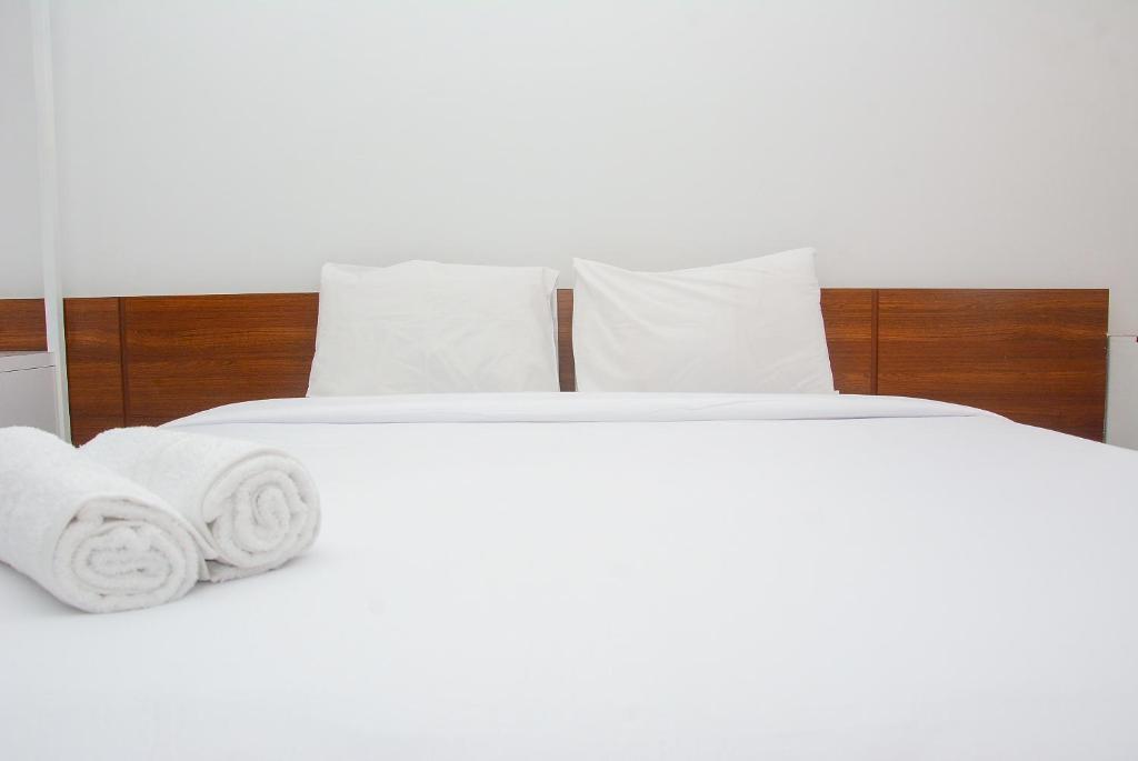 ein weißes Bett mit weißen Kissen und Handtüchern darauf in der Unterkunft Comfy Studio Room at Patraland Urbano Apartment By Travelio in Bekasi