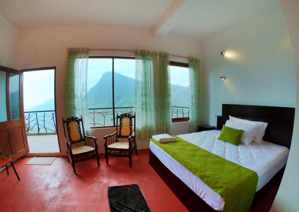 a bedroom with a bed and two chairs and a large window at Ella Ravana Seetha Mountain View Villa in Ella