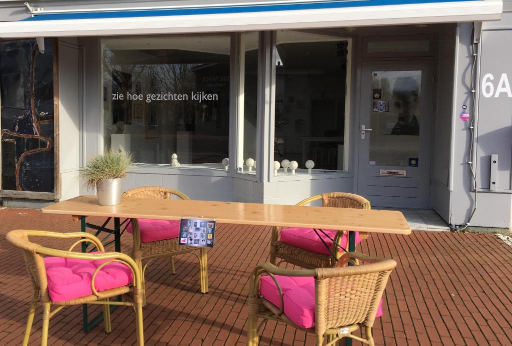 una mesa de madera y sillas con cojines rosas en el patio en B&B De Kunstpraktijk en Veldhoven