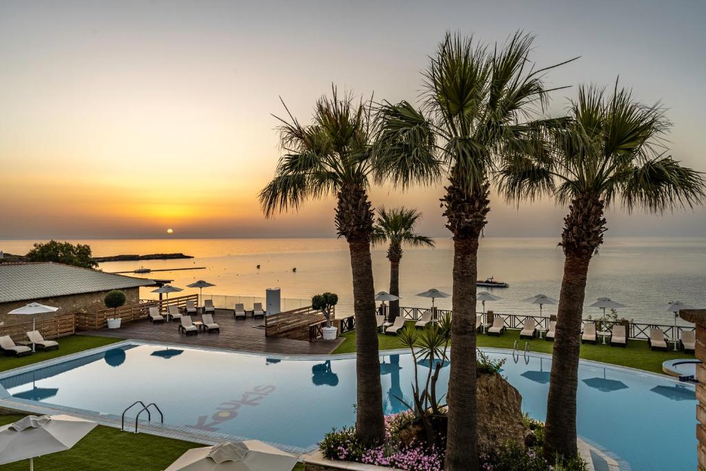a pool with palm trees and the ocean at sunset at Koukis club in Vasilikos