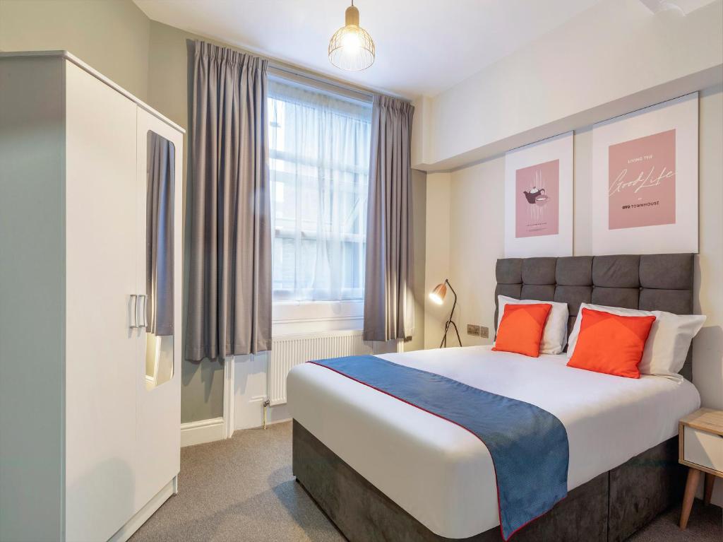 Townhouse Apollo, Hyde Park في لندن: غرفة نوم مع سرير كبير مع وسائد برتقالية وزرقاء