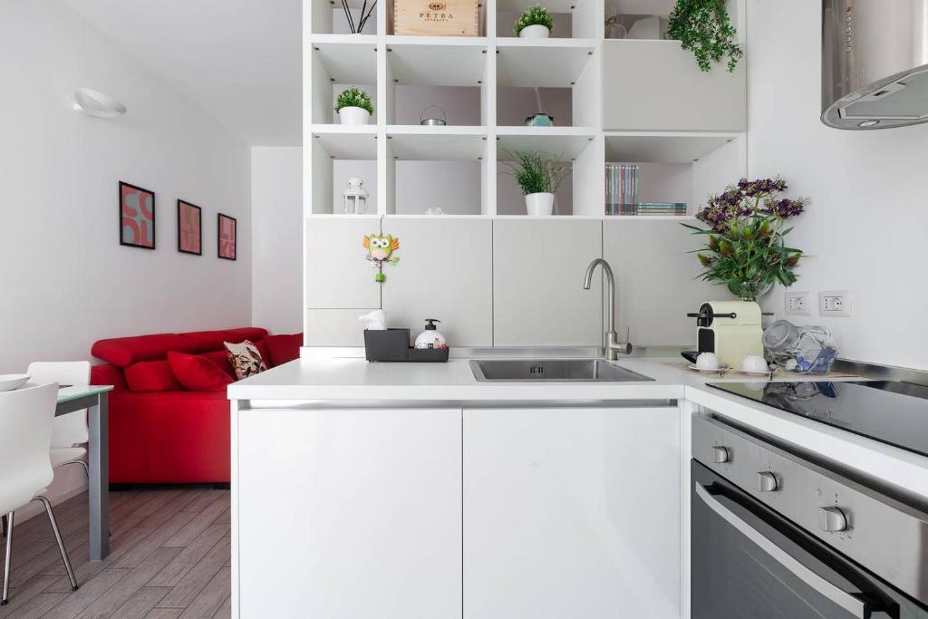 a white kitchen with a sink and a red couch at Stupendo e accogliente apt (15 min dal Duomo) in Milan