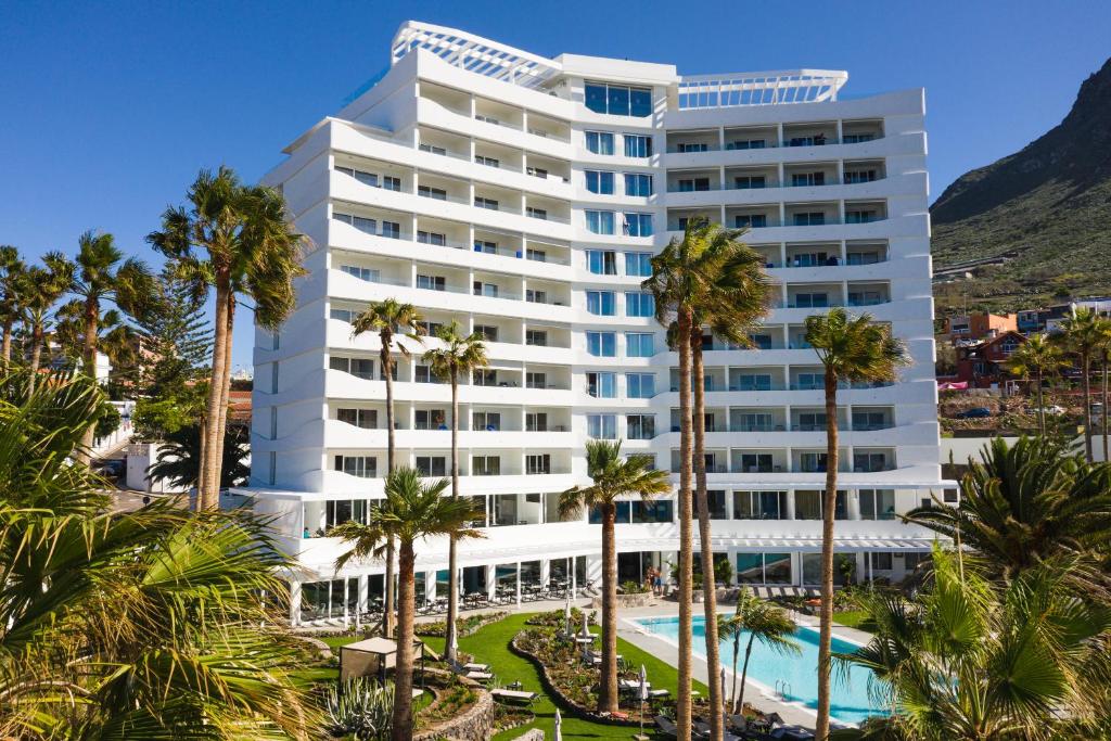 een groot wit gebouw met palmbomen en een zwembad bij OCEANO Health Spa Hotel in Punta del Hidalgo