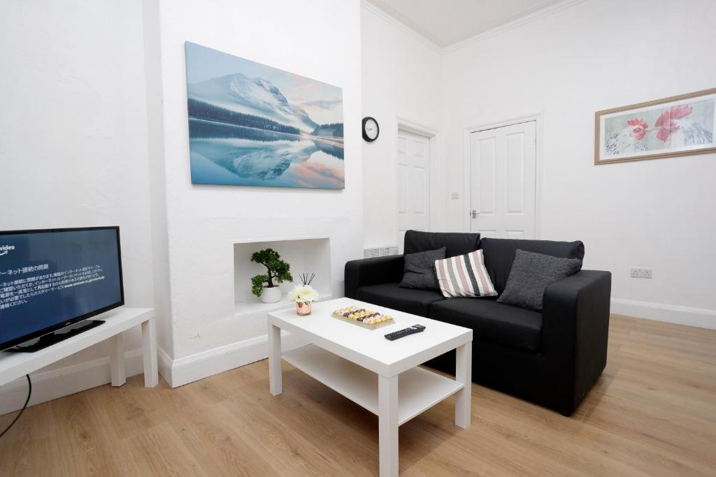 a living room with a black couch and a white coffee table at KIRKSTALL SERVICED APARTMENTS LEEDS in Leeds