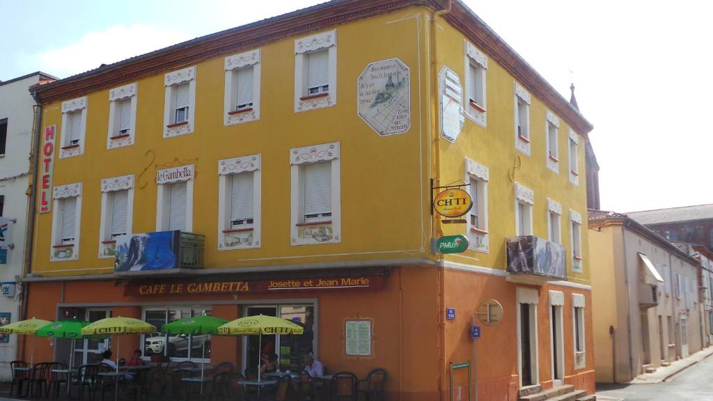 um edifício amarelo com mesas e guarda-sóis numa rua em Hotel Le Gambetta em Carmaux