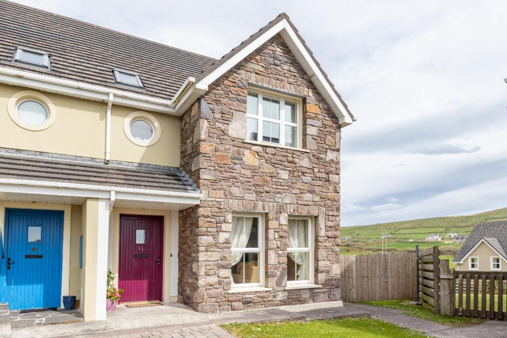 uma casa de pedra com uma porta vermelha e uma cerca em Cois Chnoic em Dingle