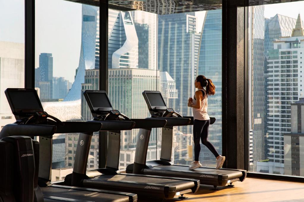 A treadmill-lined gym with floor-to-ceiling windows overlooking Bangkok towers.