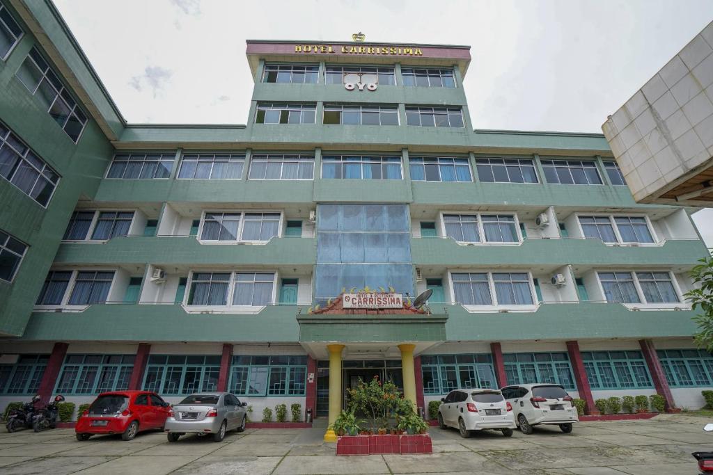 een groot groen gebouw met auto's geparkeerd voor het bij Super OYO 1389 Hotel Carissima in Palembang