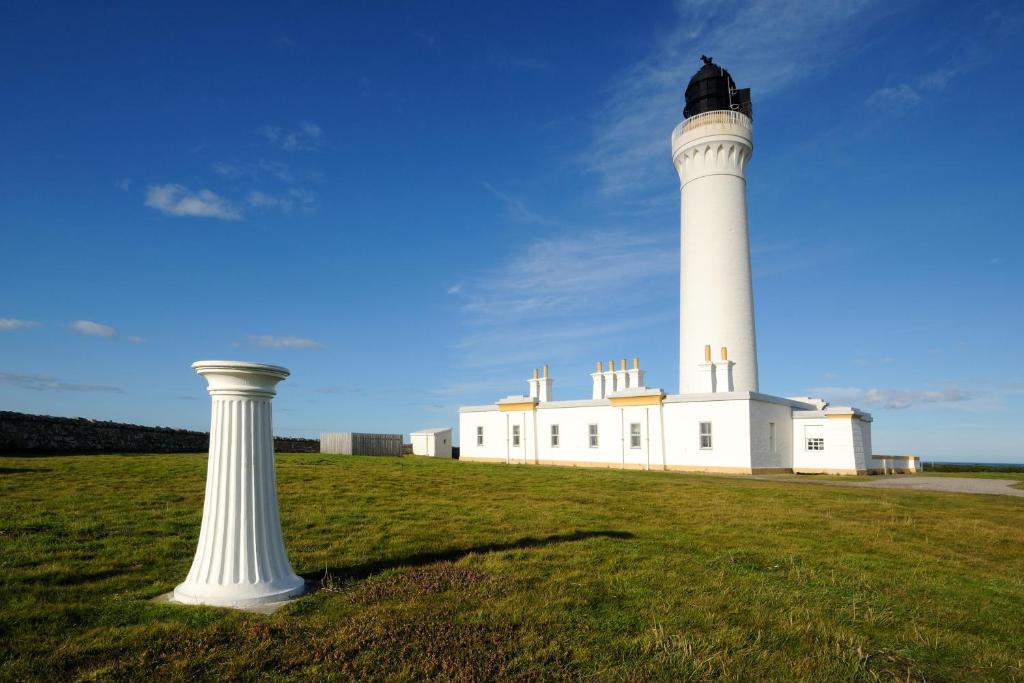 a white lighthouse on a grass field with a pole at Covesea Lighthouse Cottages in Lossiemouth