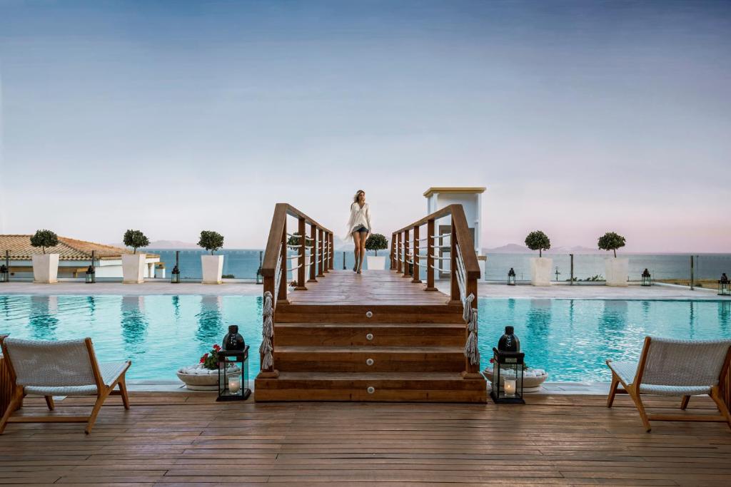 a woman walking down a wooden bridge over a pool at Mitsis Selection Blue Domes in Kardamaina