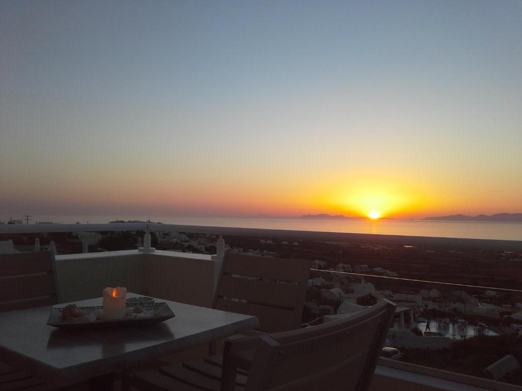 a sunset from a balcony with a table and chairs at Kiklamino Sunset Studios in Oia