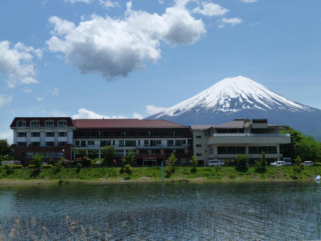 una montaña en el fondo con un edificio y un cuerpo de agua en Lakeland Hotel Mizunosato, en Fujikawaguchiko