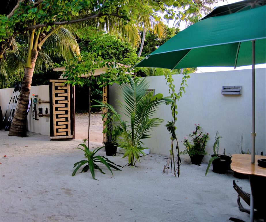 un patio con una mesa y una sombrilla verde en Kuri Beach View Inn, en Omadhoo