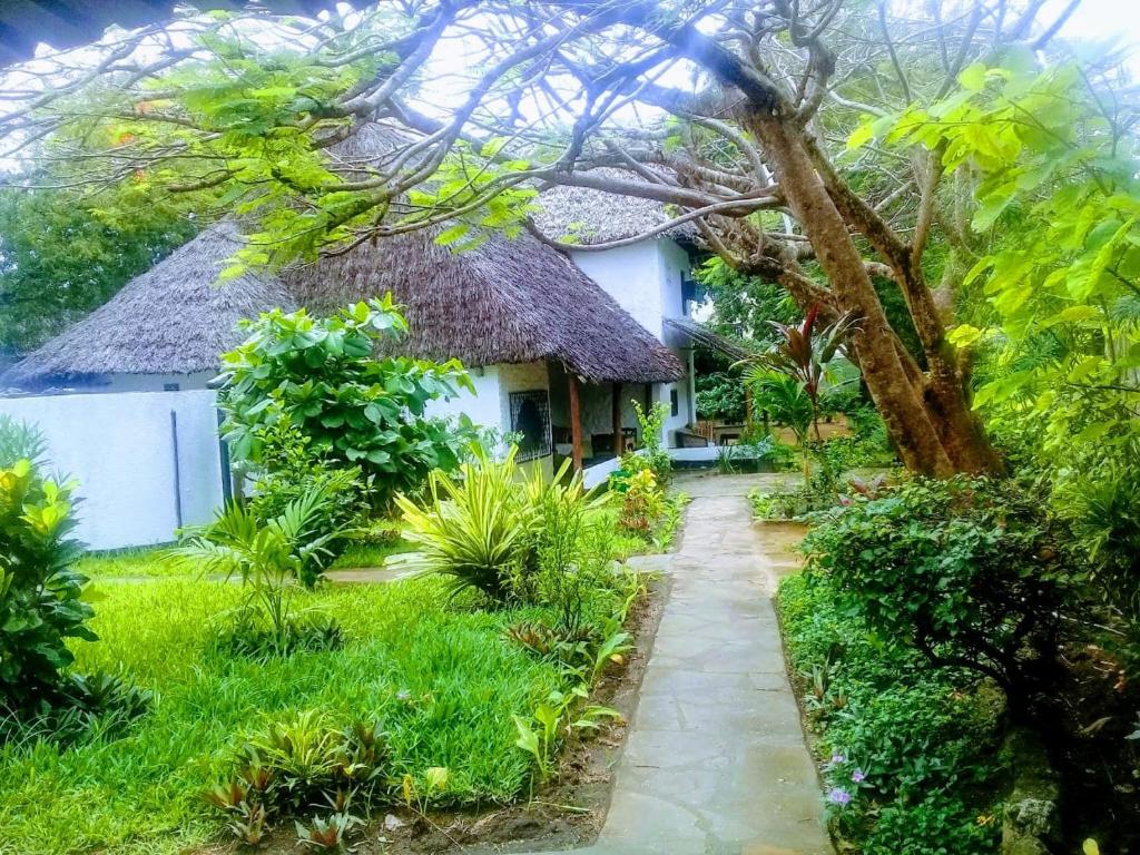 a house with a thatched roof and a walkway at Diani Banda Cottages in Diani Beach