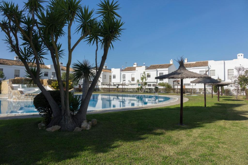 a swimming pool with two palm trees and an umbrella at Casa Real la Barrosa in Chiclana de la Frontera