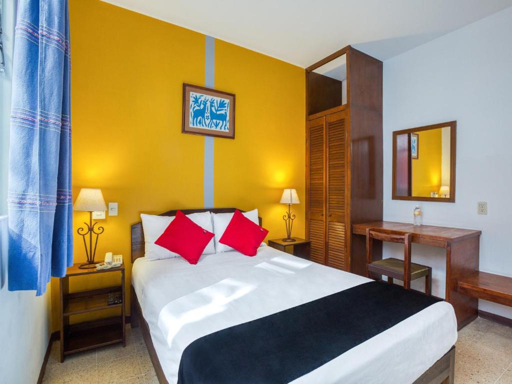1 dormitorio con 1 cama grande con almohadas rojas en Capital O Parador Crespo Hotel, Oaxaca en Oaxaca de Juárez