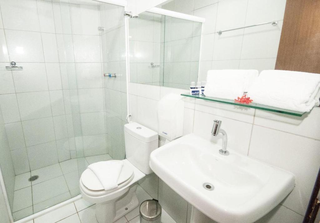 a white bathroom with a toilet and a sink at Hotel Enseada Boa Viagem in Recife