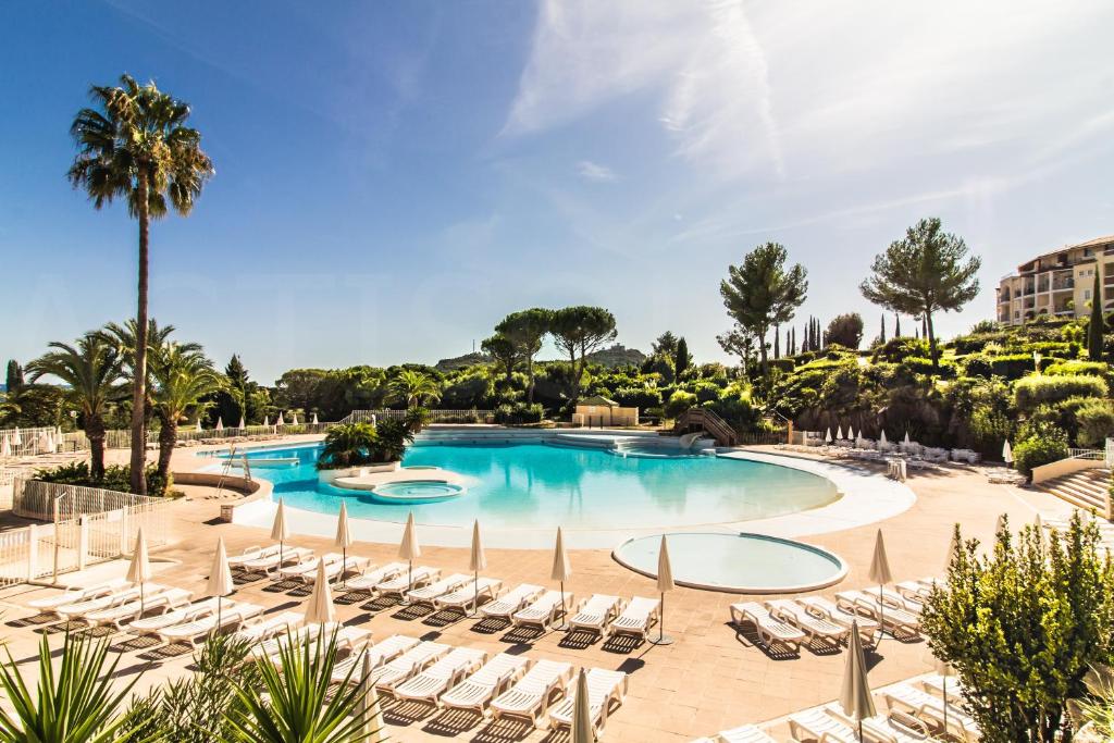 a large swimming pool with chairs and palm trees at Cap Estérel by Actisource in Agay - Saint Raphael